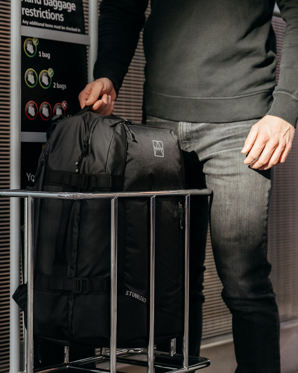 A man placing an All Black Adventure Bag into the bag size checker at an airport