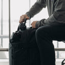 A man putting his head phones into the top pocket on an All Black Adventure Bag