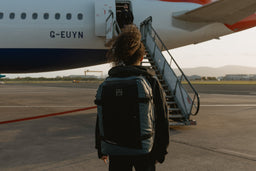 A woman walking towards an airplane at the airport wearing a Tasmin Blue Adventure Bag