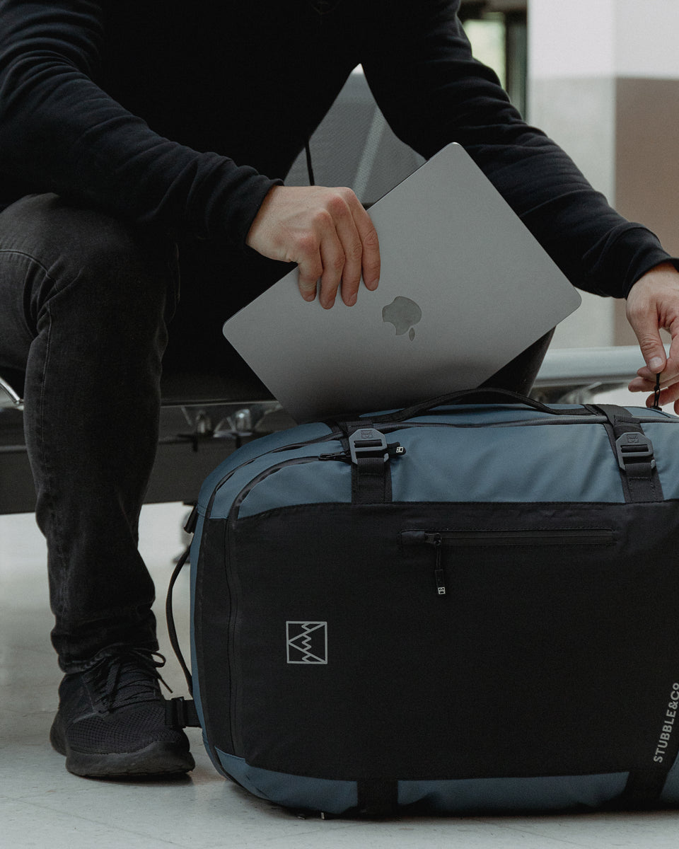 a Tasmin Blue adventure bag on the floor with a man putting a laptop into the laptop compartment