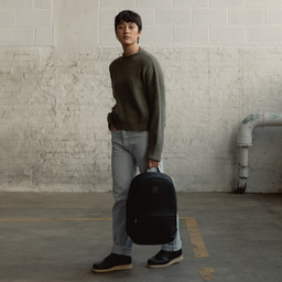 A woman standing holding a Classic Backpack 15L in All Black down by her side