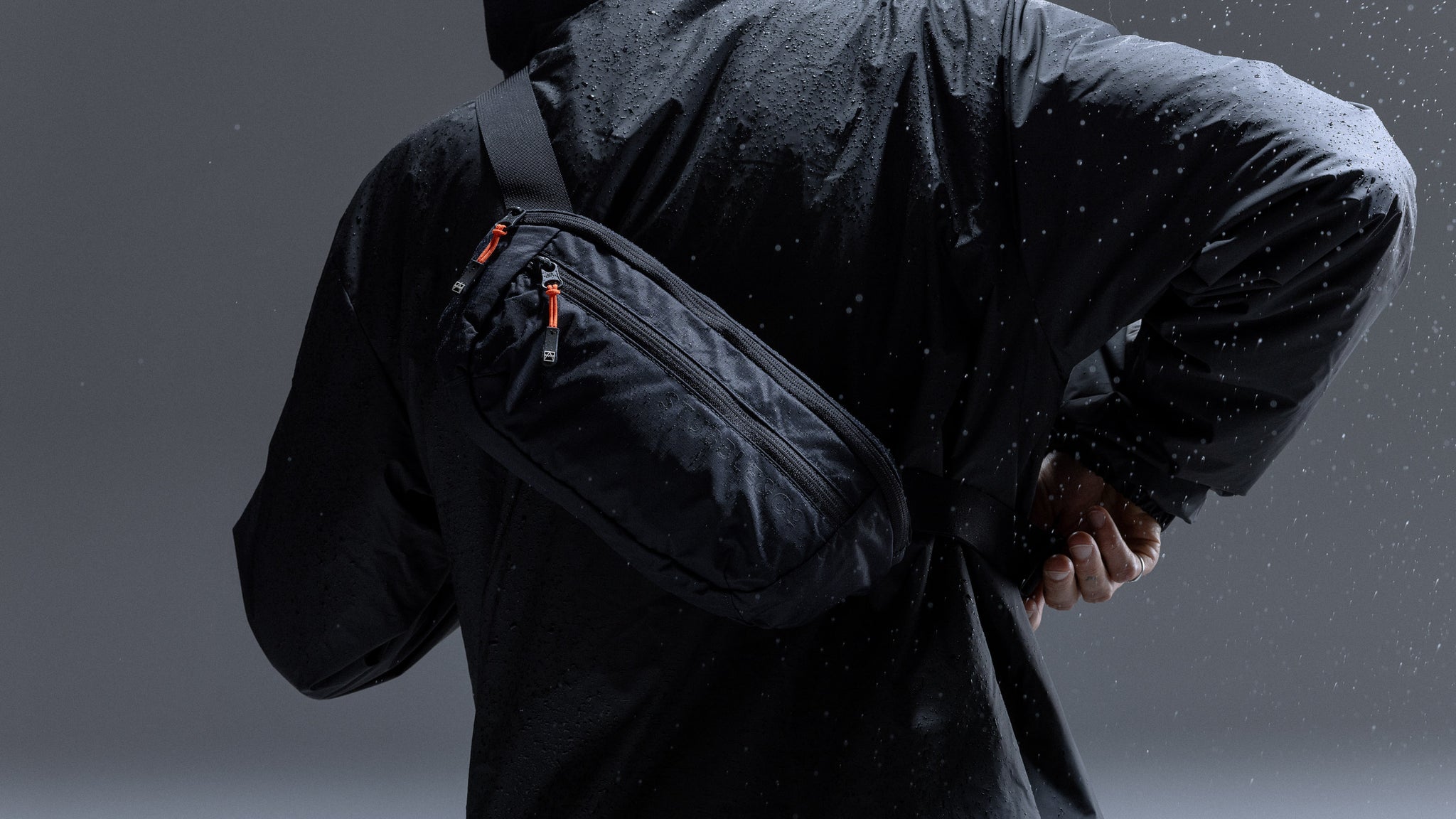 a studio shot of a man wearing a packable sling with water spraying onto it