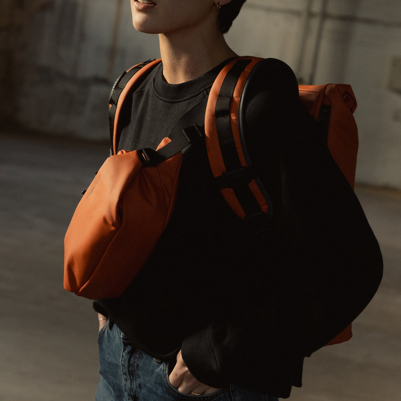 A close up of a woman wearing a Roll Top on her back and Crossbody in Rust on her front