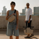 a man holding a tote bag by his side behind a man wearing a Sand Crossbody on her chest