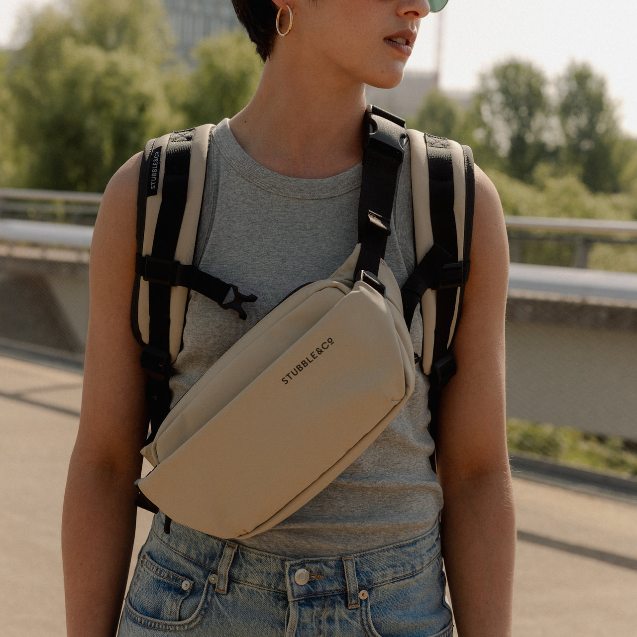 A close up shot of a woman wearing a Sand Crossbody and roll top backpack