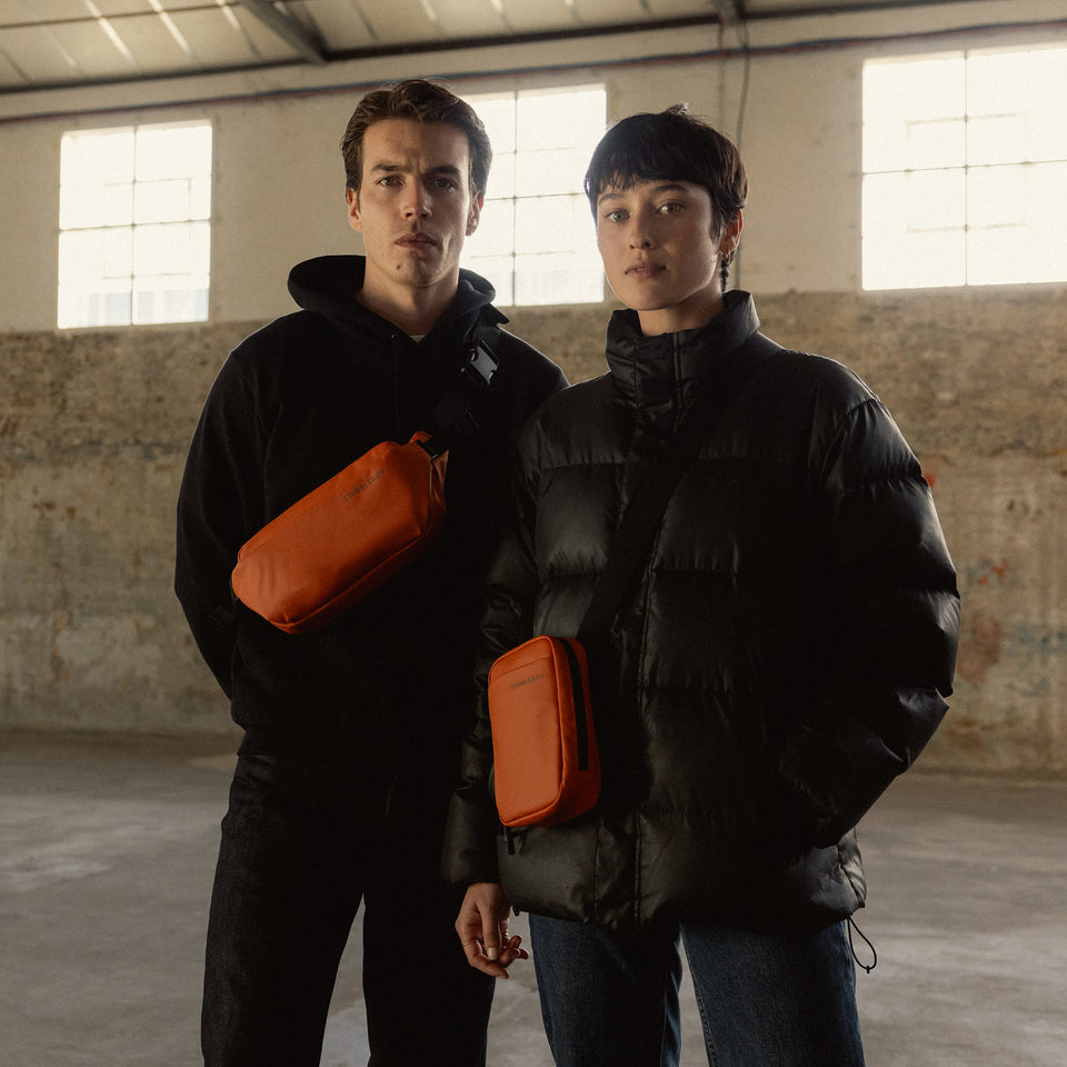 A man wearing a crossbody and woman wearing a shoulder bag in Rust