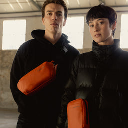 A man wearing a Crossbody and woman wearing a Shoulder Bag in Rust