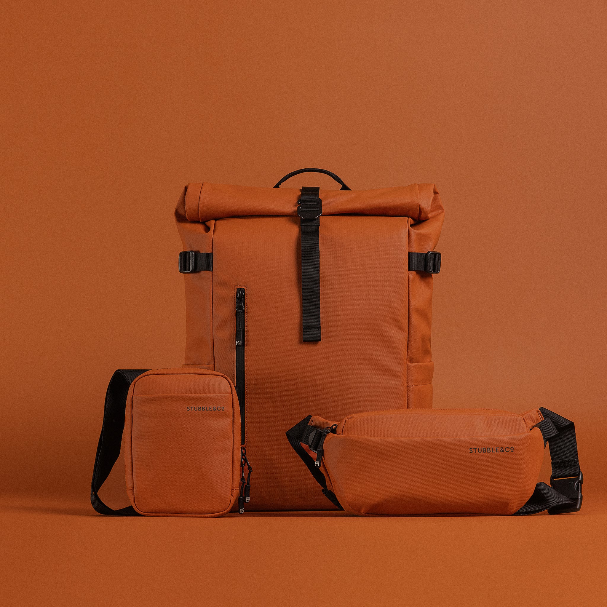 A studio shot of the Rust collection including the Roll Top, Shoulder Bag and Crossbody on a Rust background