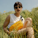 a woman sitting on the grass whilst wearing a Yellow crossbody