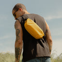 a man standig in a field facing away with a Yellow crossbody on his back