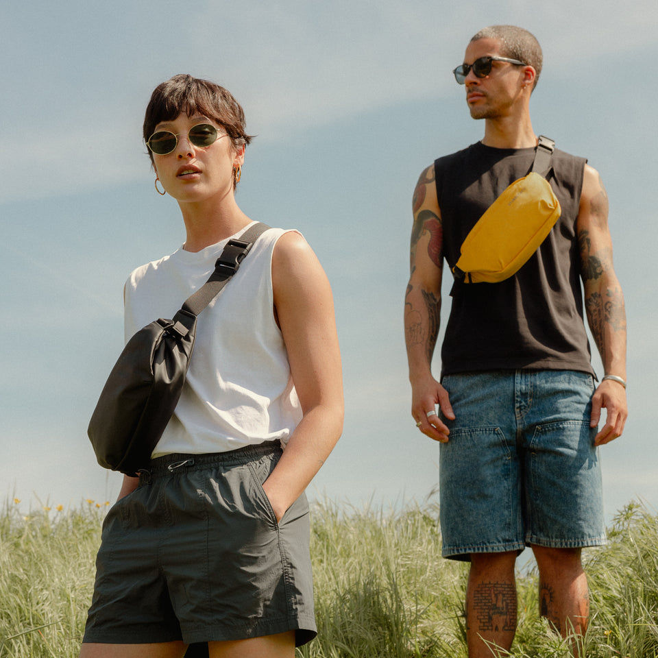 a man and woman standing in a field wearing a Yellow crossbody on their front