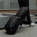 A Everyday Backpack 15L in All Black being wheeled on a suitcase using its luggage sleeve