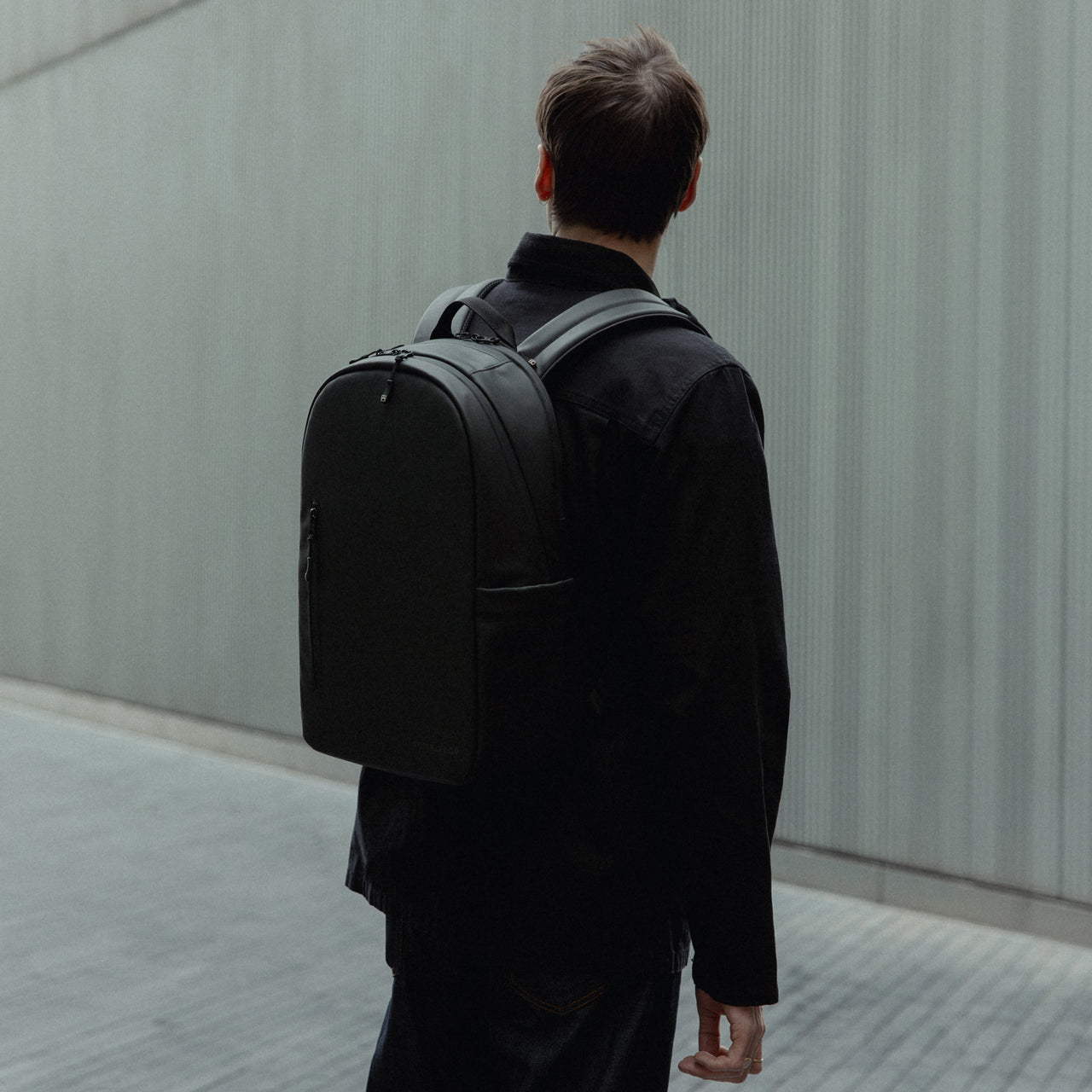 A man facing away wearing an All Black Everyday Backpack 15L on his back