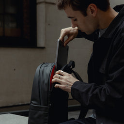 A man putting away his laptop in the compartment of an Everyday Backpack 15L in All Black