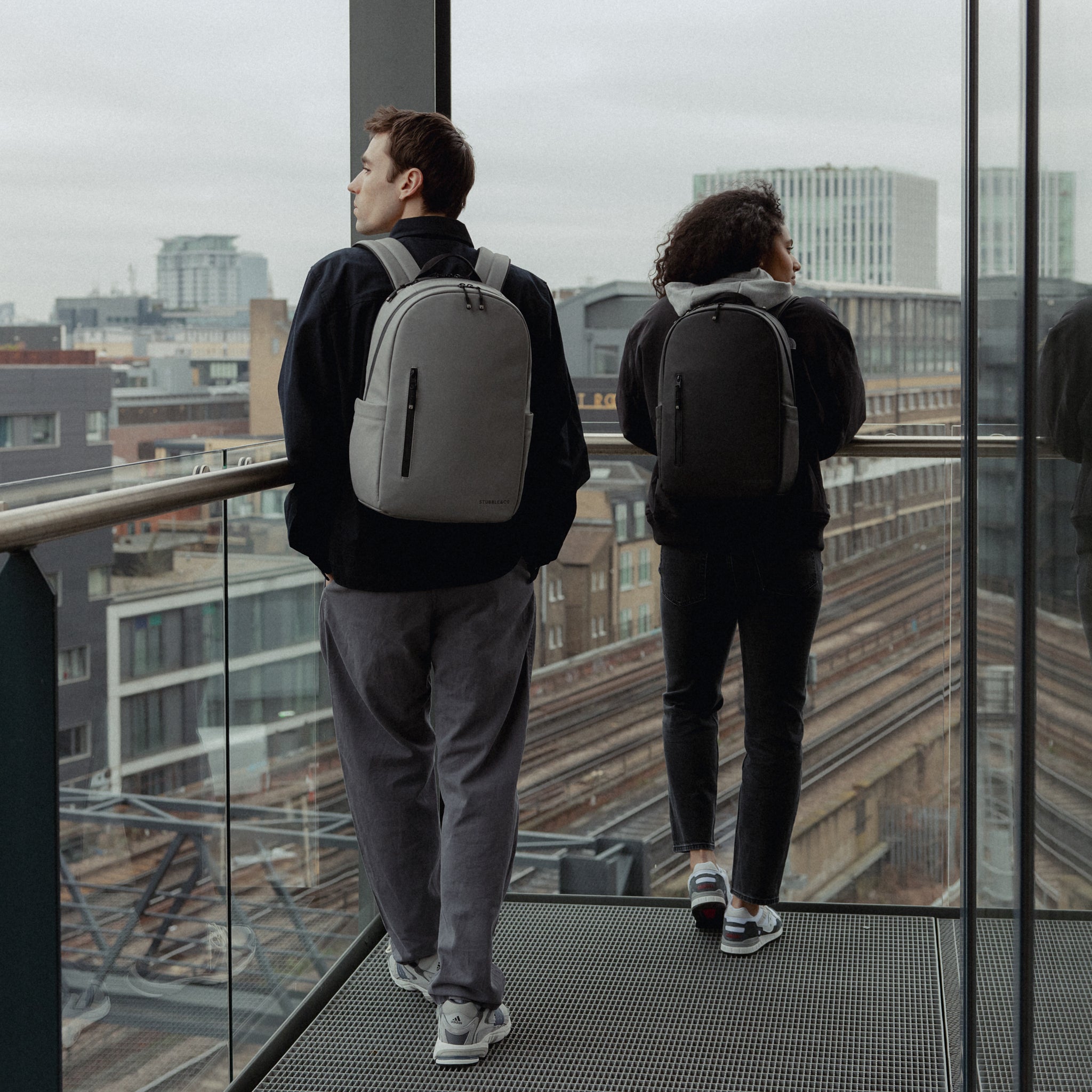 A man and woman wearing Everyday Backpack15L on their backs in black and Concrete