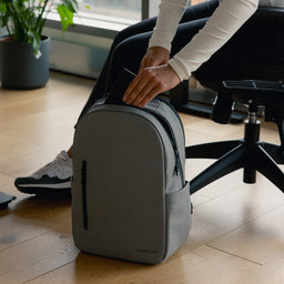 A woman putting a book into an Everyday Backpack 15L in Concrete