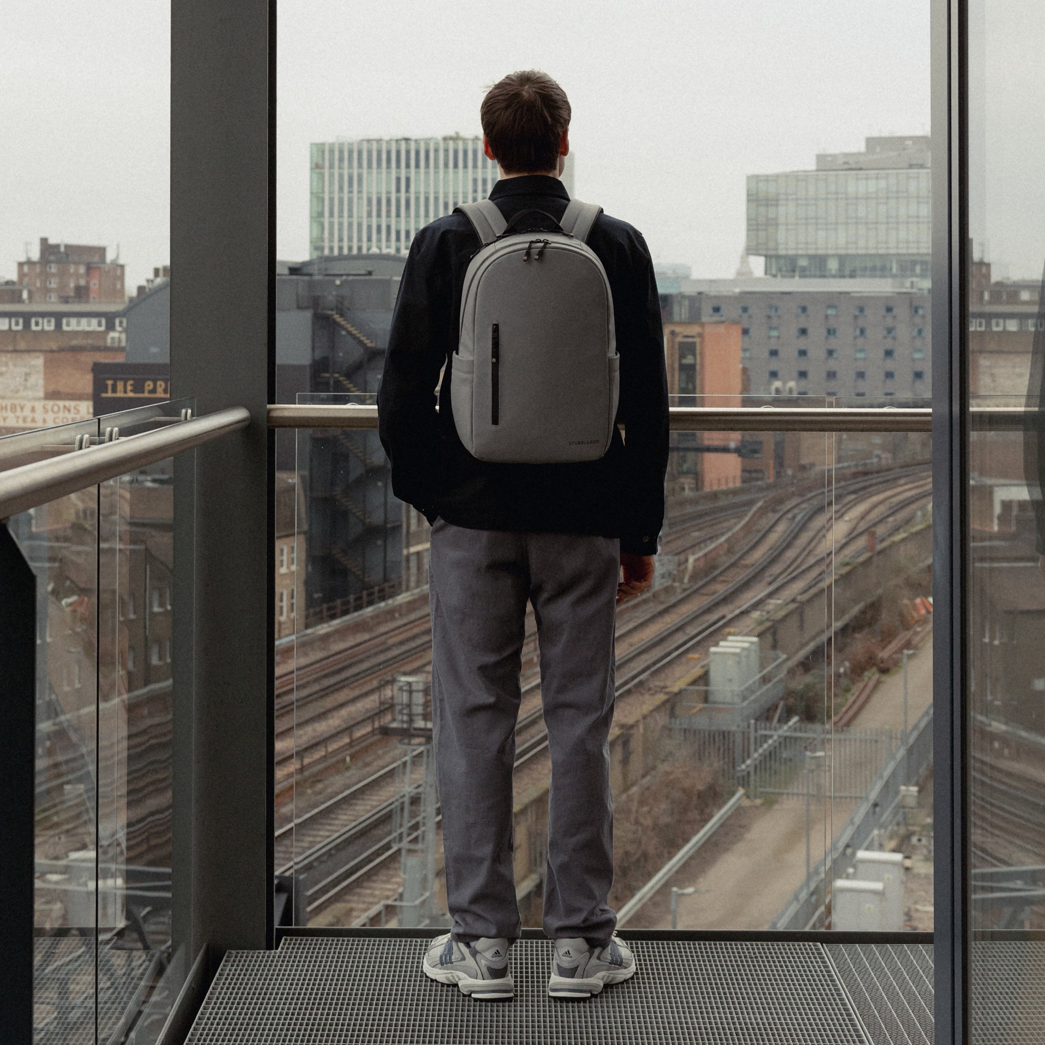 A man standing on a balcony wearing an Everyday Backpack 15L on his back in Concrete