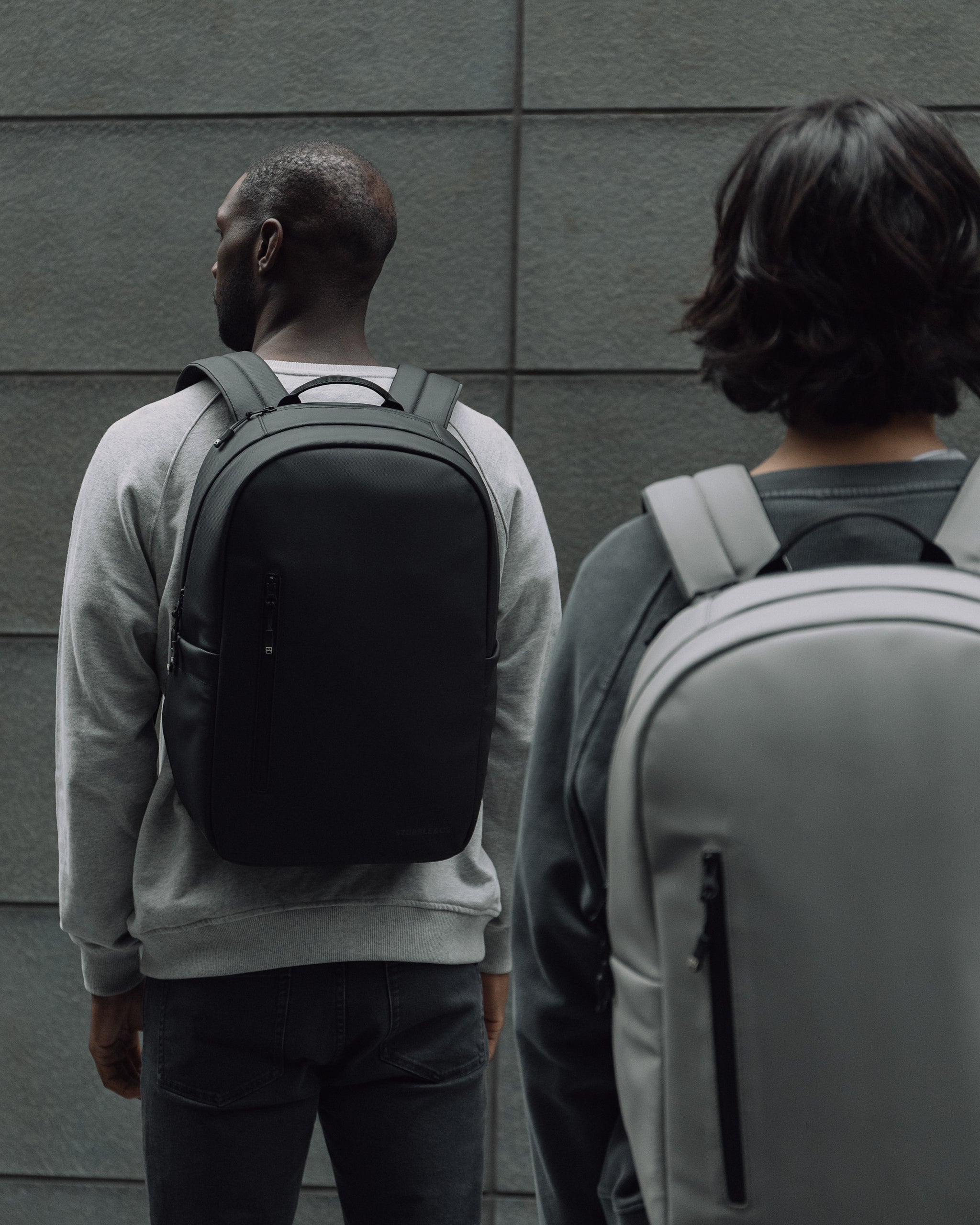 a man and woman wearing everyday backpack on their back facing away from the camera