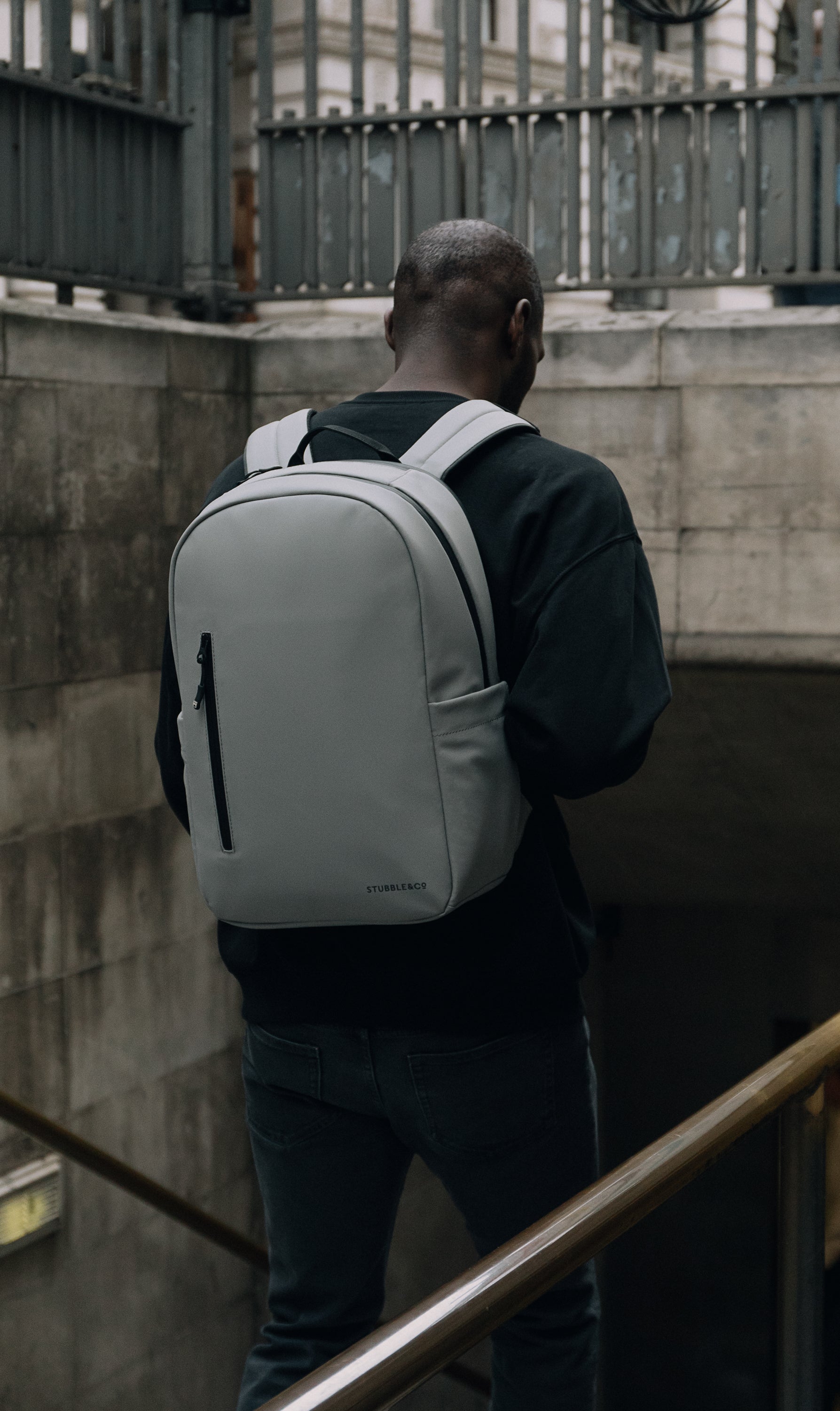 A man wearing a concrete everyday backpack on his back as he walks down the stairs to the tube in Londond