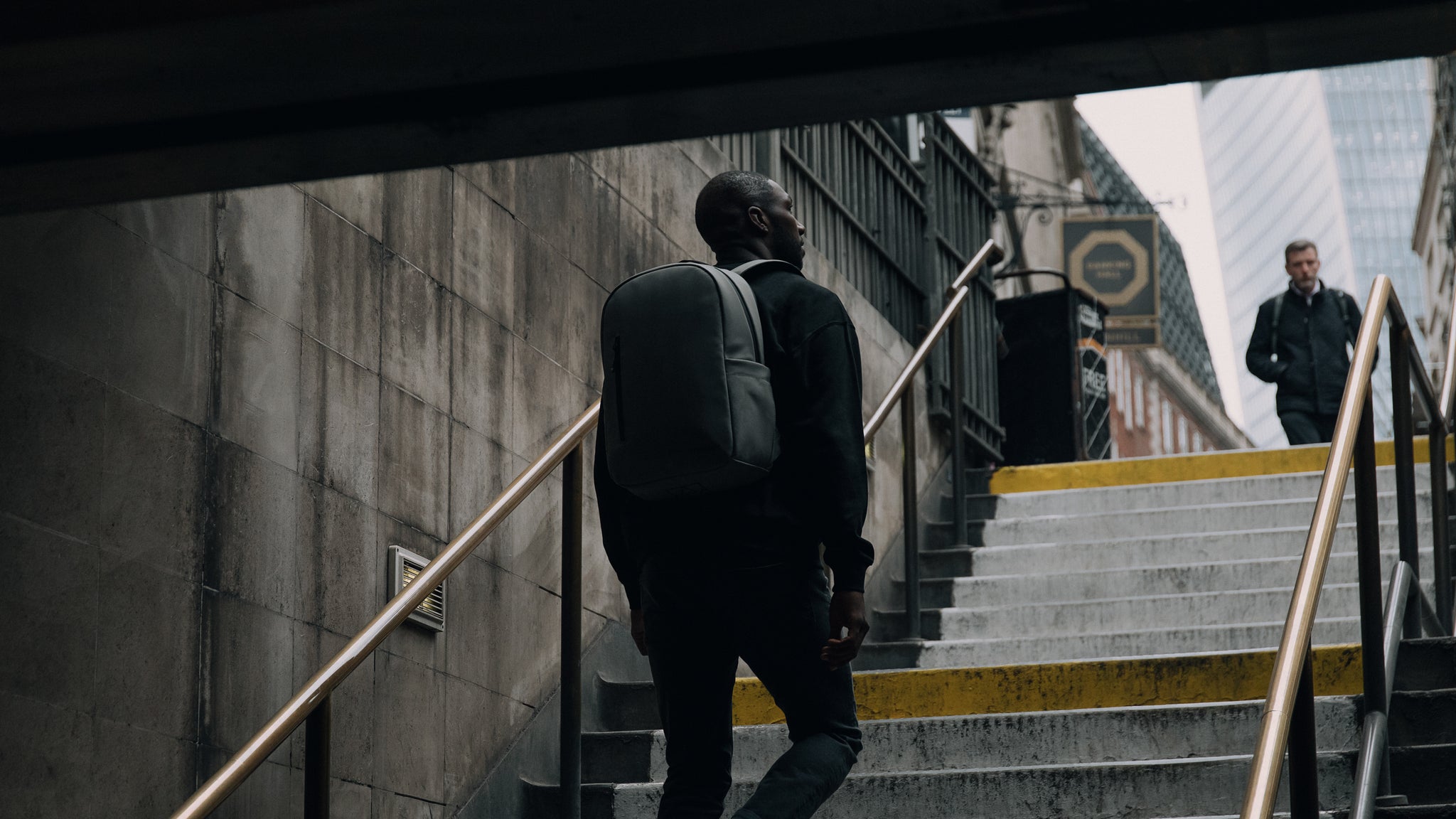 A man walking out of the tube station wearing a concrete everyday backpack on his back