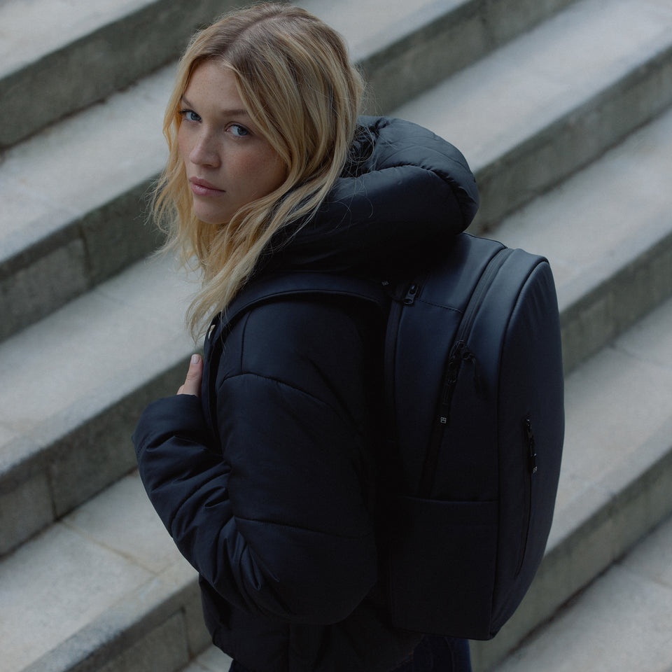 A woman walking up the stairs with an Everyday Backpack in Midnight Blue on her back