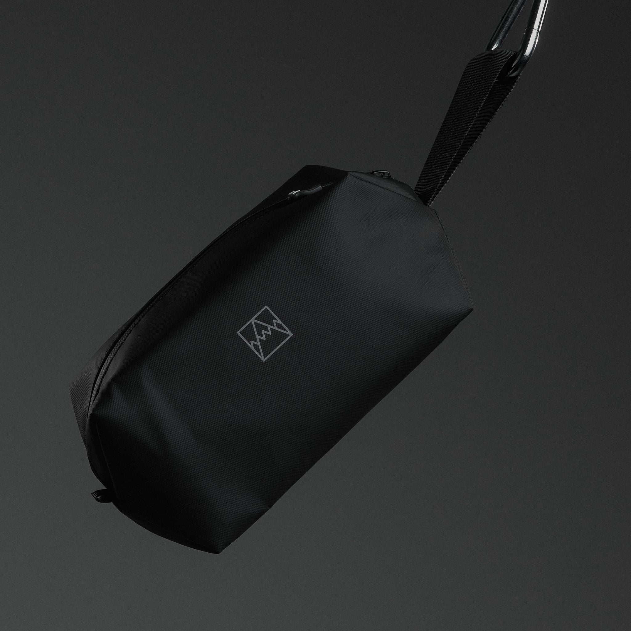 A studio shot of a wash bag hanging by its grab handle with a carabener