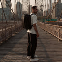 A lifestyle shot of a man standing on Brooklyn Bridge in New york with a  Hybrid Backpack 30L in All Black on his back