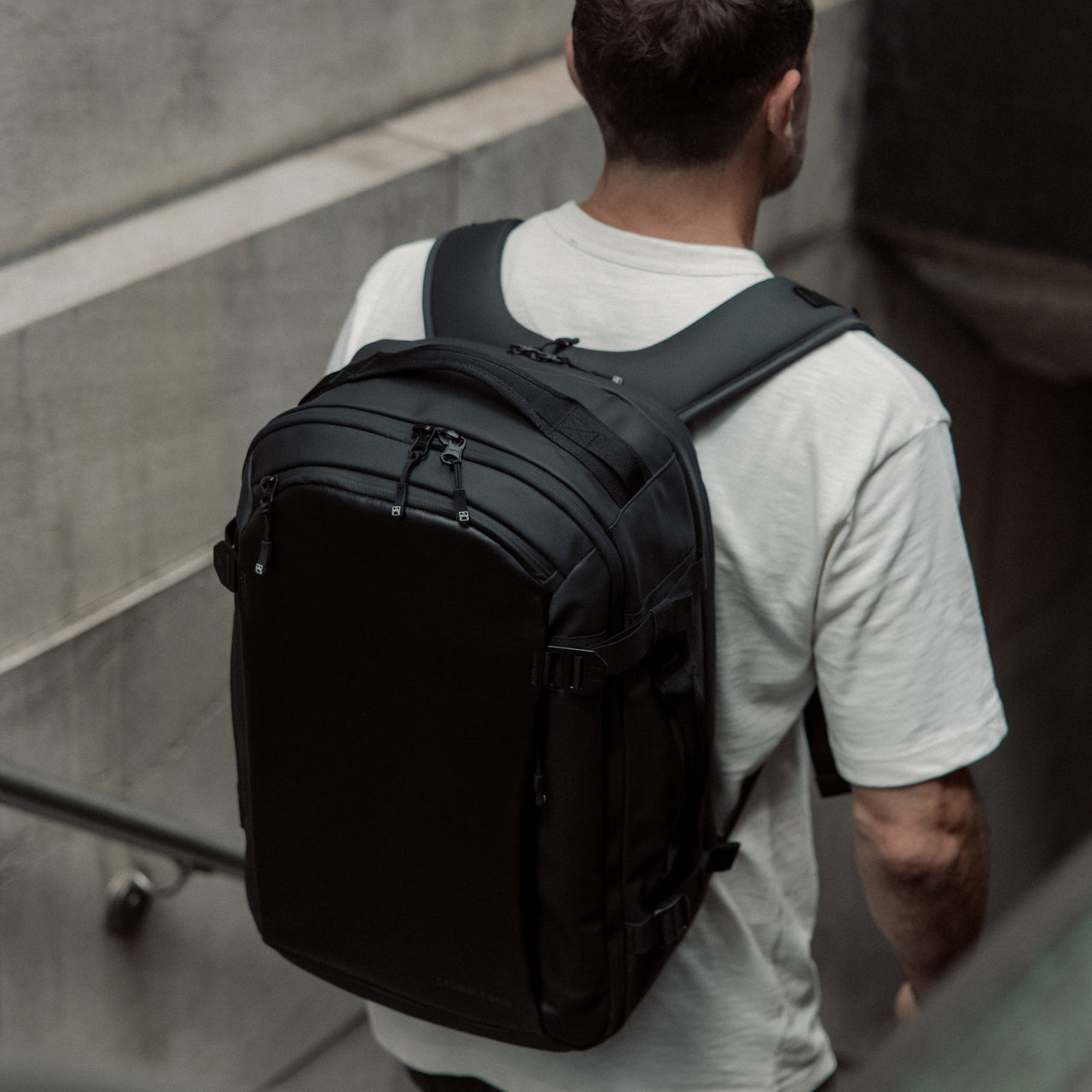 A lifestyle shot of a man walking into the subway in New York with a  Hybrid Backpack 30L in All Black on his back