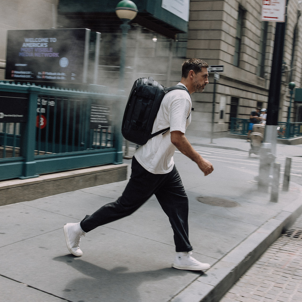 A lifestyle shot of a man crossing the road in New York with a  Hybrid Backpack 30L in All Black on his back