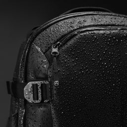 A cretive studio shot of the top corner of the  Hybrid Backpack 30L in All Black with water droplets on the waterproof materials