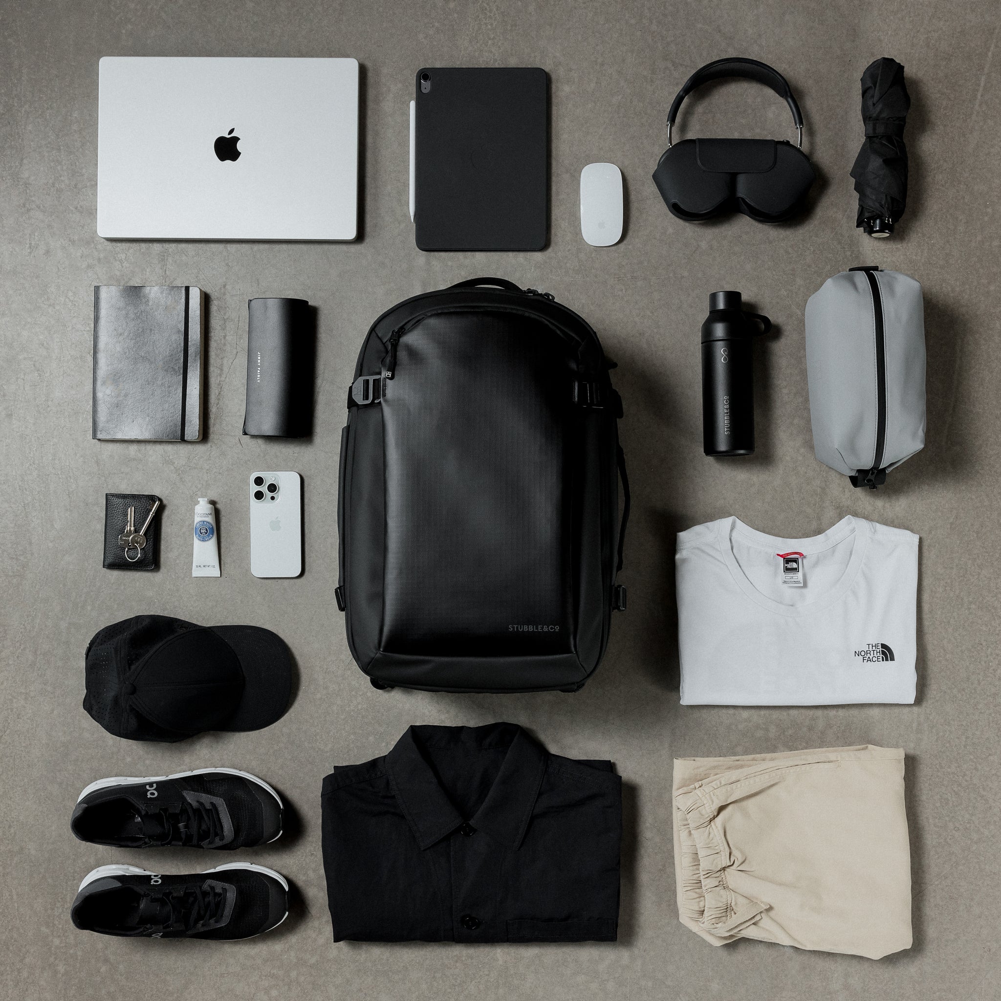 A creative studio flat lay of the  Hybrid Backpack 30L in All Black, surrounded by items of daily life.