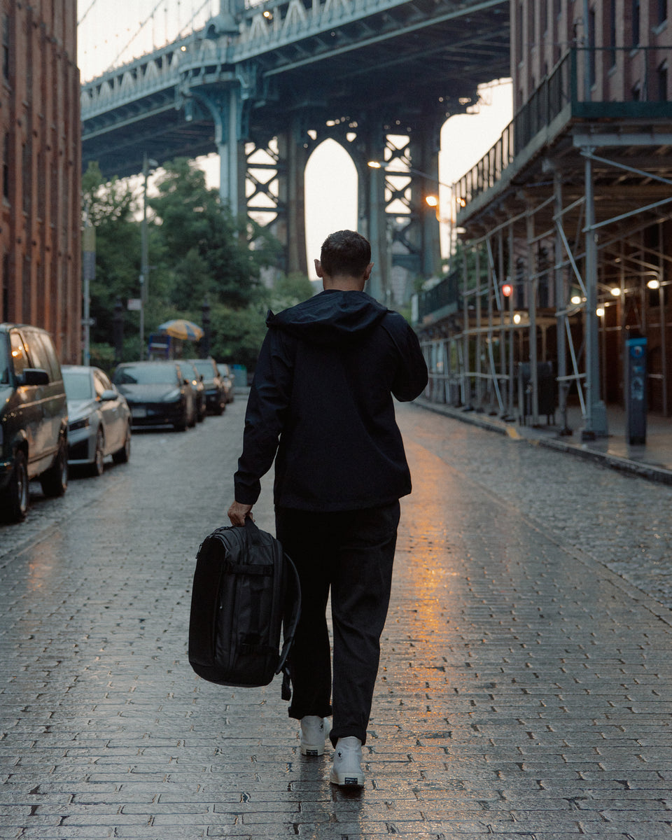 A man walking away from the camera whilst holding the Hybrid backpack 30l at his side