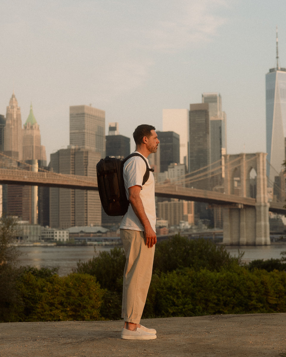 a man standing parallell to the camera with the New York skyline in the background whilst wearing a Hybrid Backpack 30L on his back