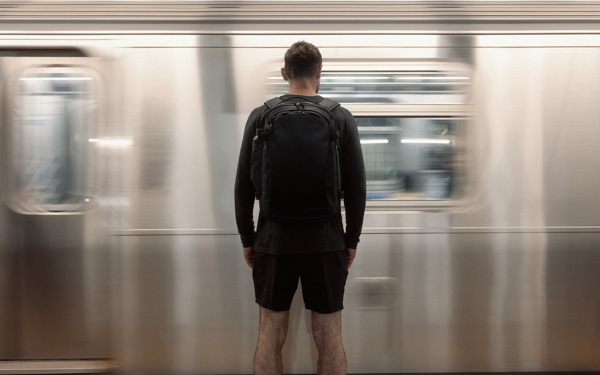 a man standing on a subway platform in New York wearing a Hybrid Backpack 30L on his back