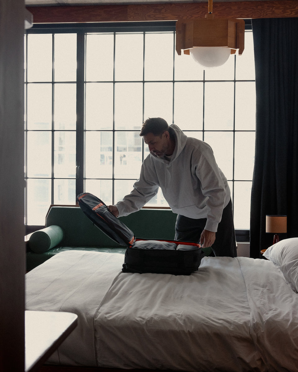 A man opening up his Hybrid backpack 30L using its clamshell design to pack it on his hotel bed