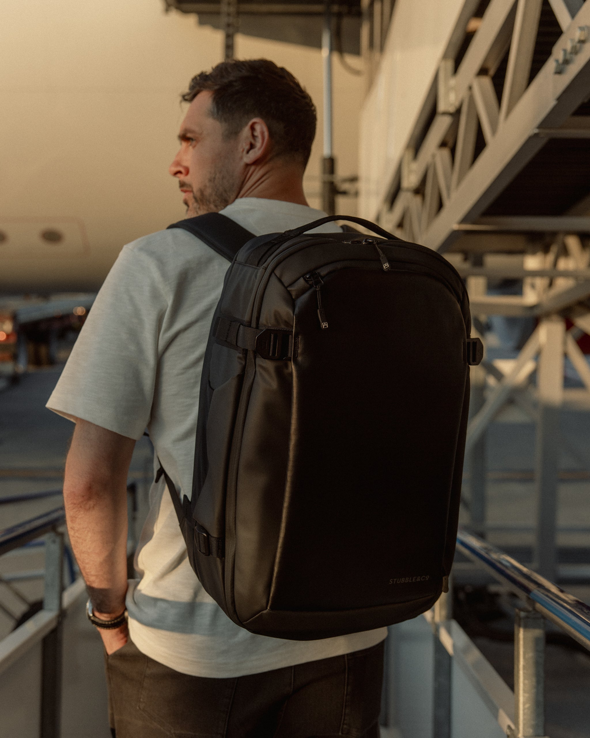 A man walking towards a plane at an airport wearing a Hybrid 30L Backpack 30L on his back