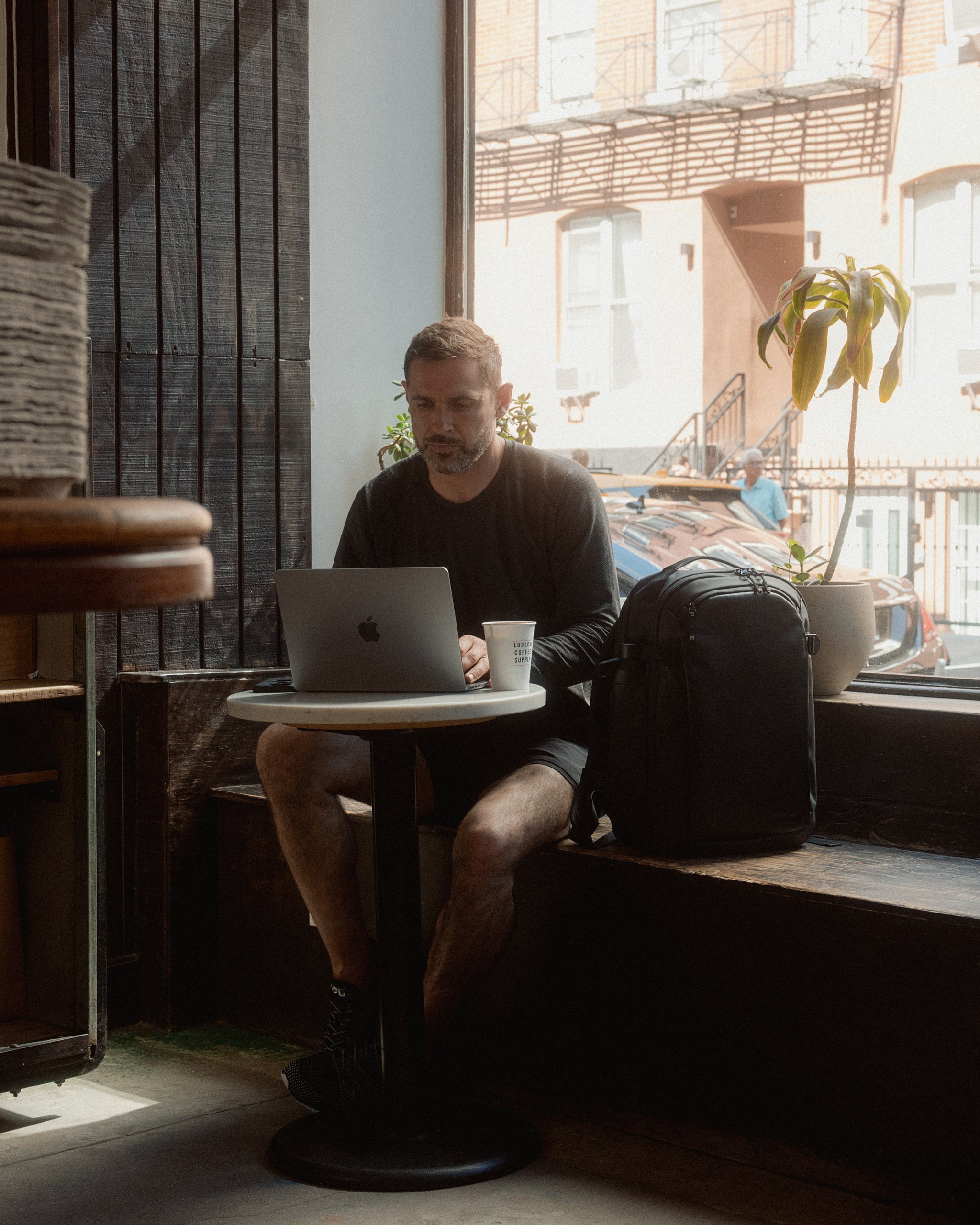 A man sitting on his laptop working in a cafe in New York with the Hybrid Backpack 30L on the seat next to him