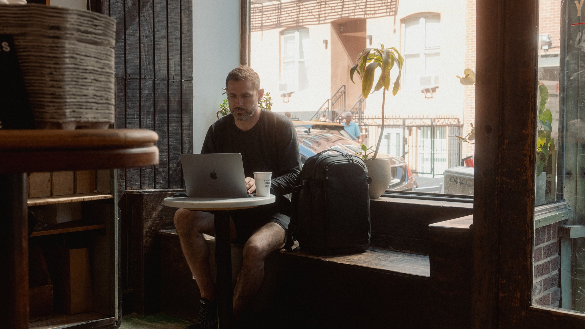 A man sitting on his laptop in a cafe with a hybrid backpack 30l on the bench next to him