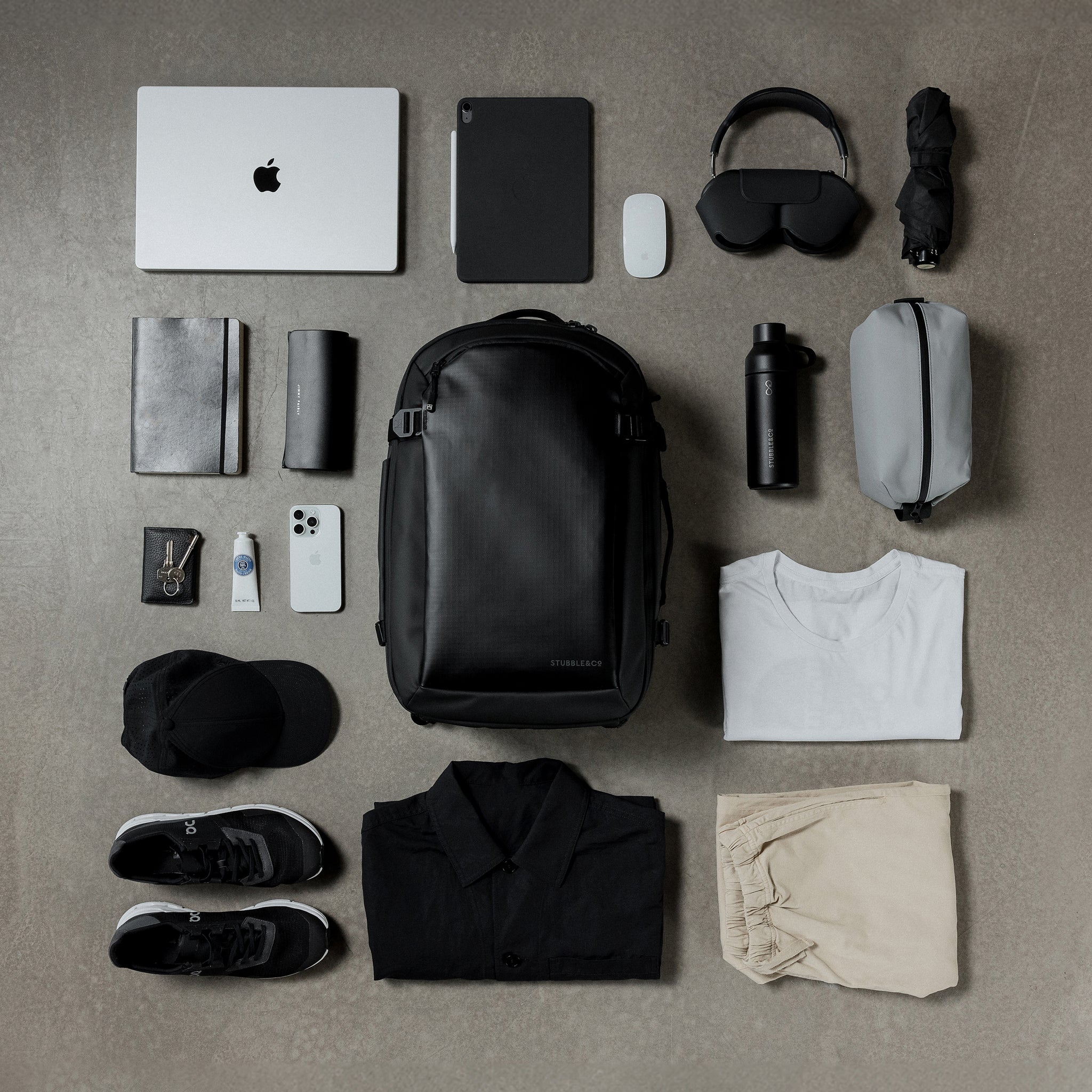 A creative studio flat lay of the  Hybrid Backpack 30L in All Black, surrounded by items of daily life.