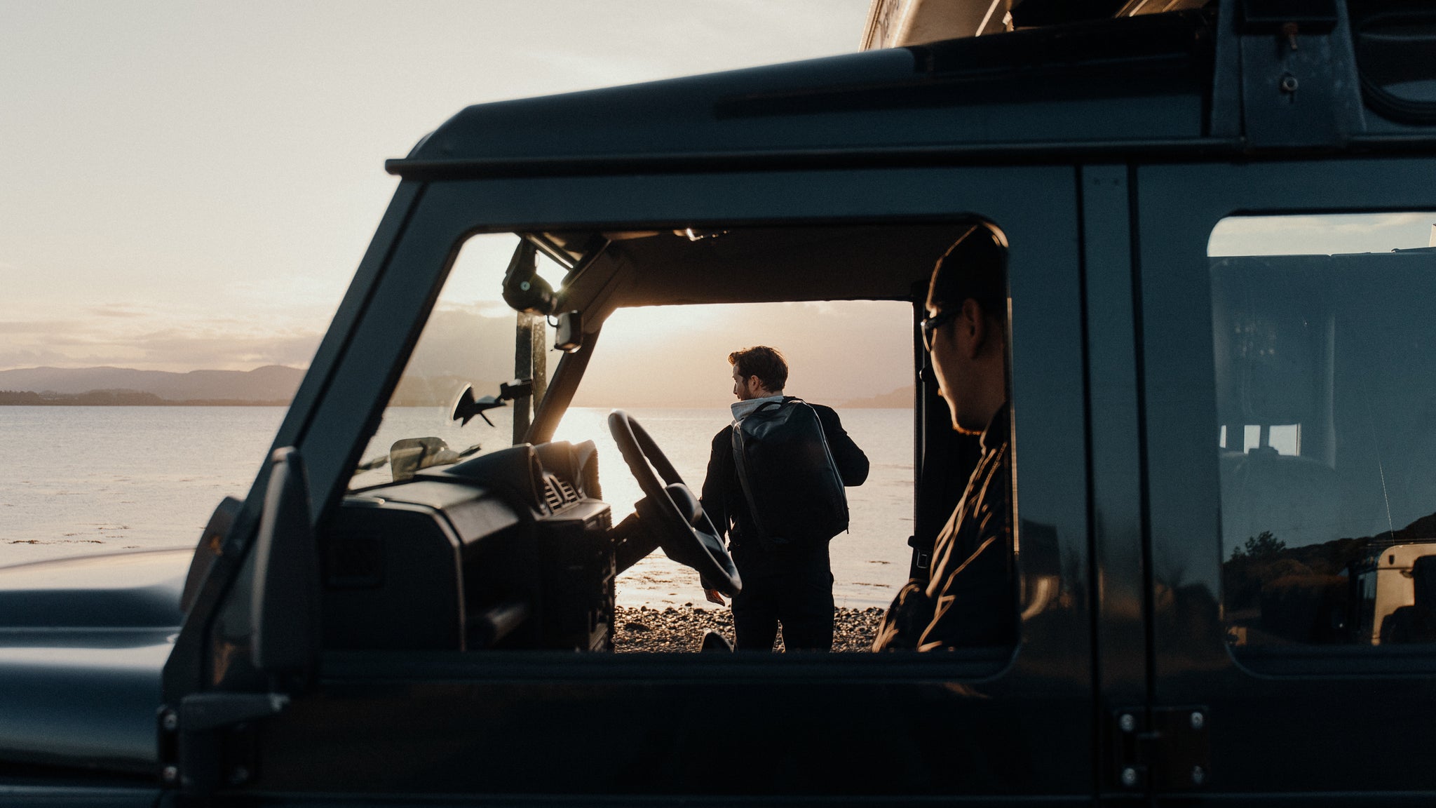 A man with a bag on his back is standing in front of a car.