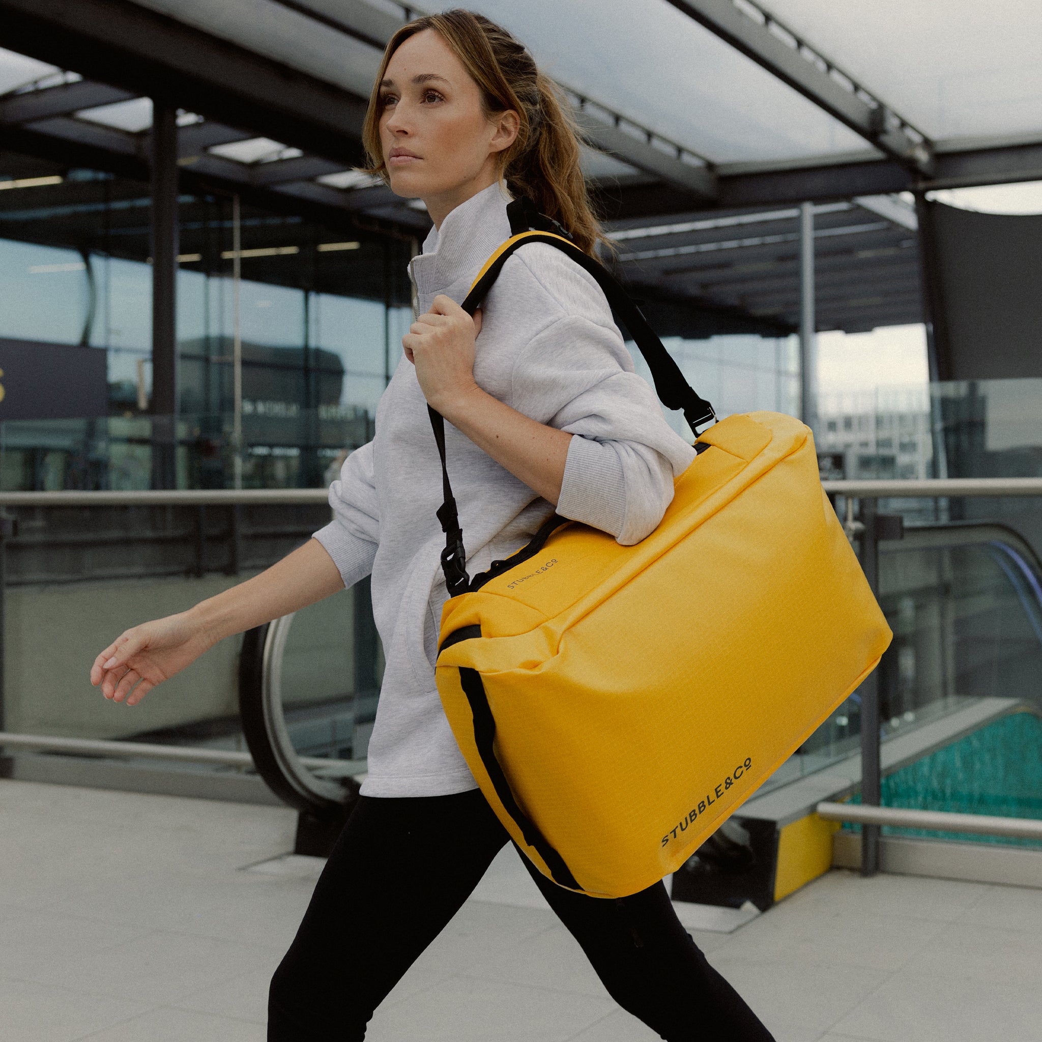 A woman walking with her a Kit Bag 30L in Yellow on her shoulder