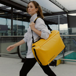 A woman walking with her a Kit Bag 30L in Yellow on her shoulder