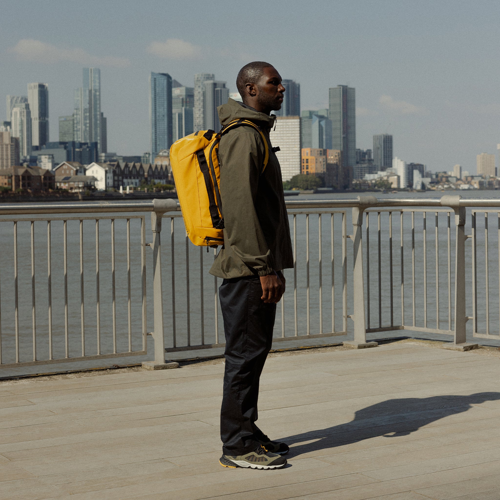 A man standing next to the river wearing a Kit Bag 30L in Yellow on his back