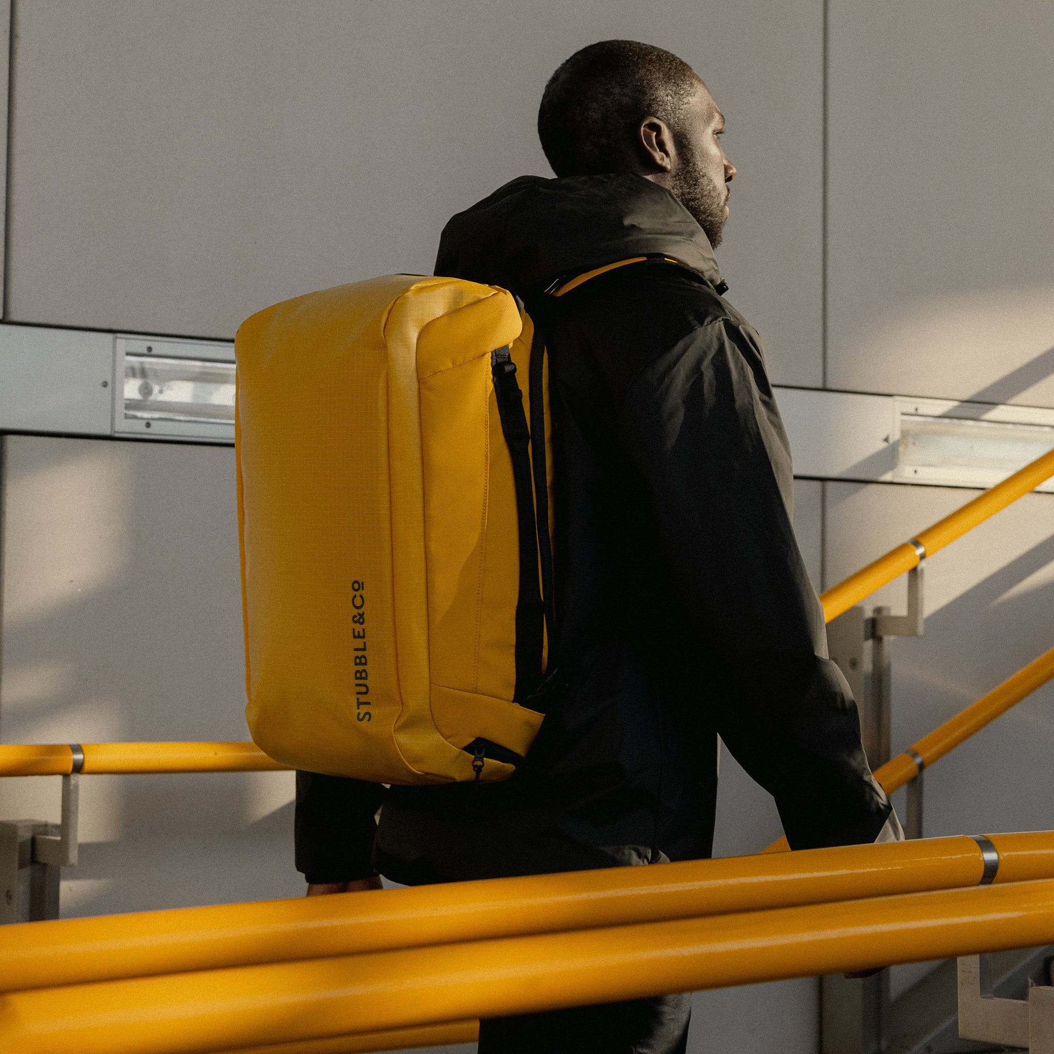 A man walking up stairs wearing a Kit Bag 30L in Yellow on his back