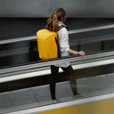 A woman standing on an escalator with a Kit Bag 30L in Yellow on her back