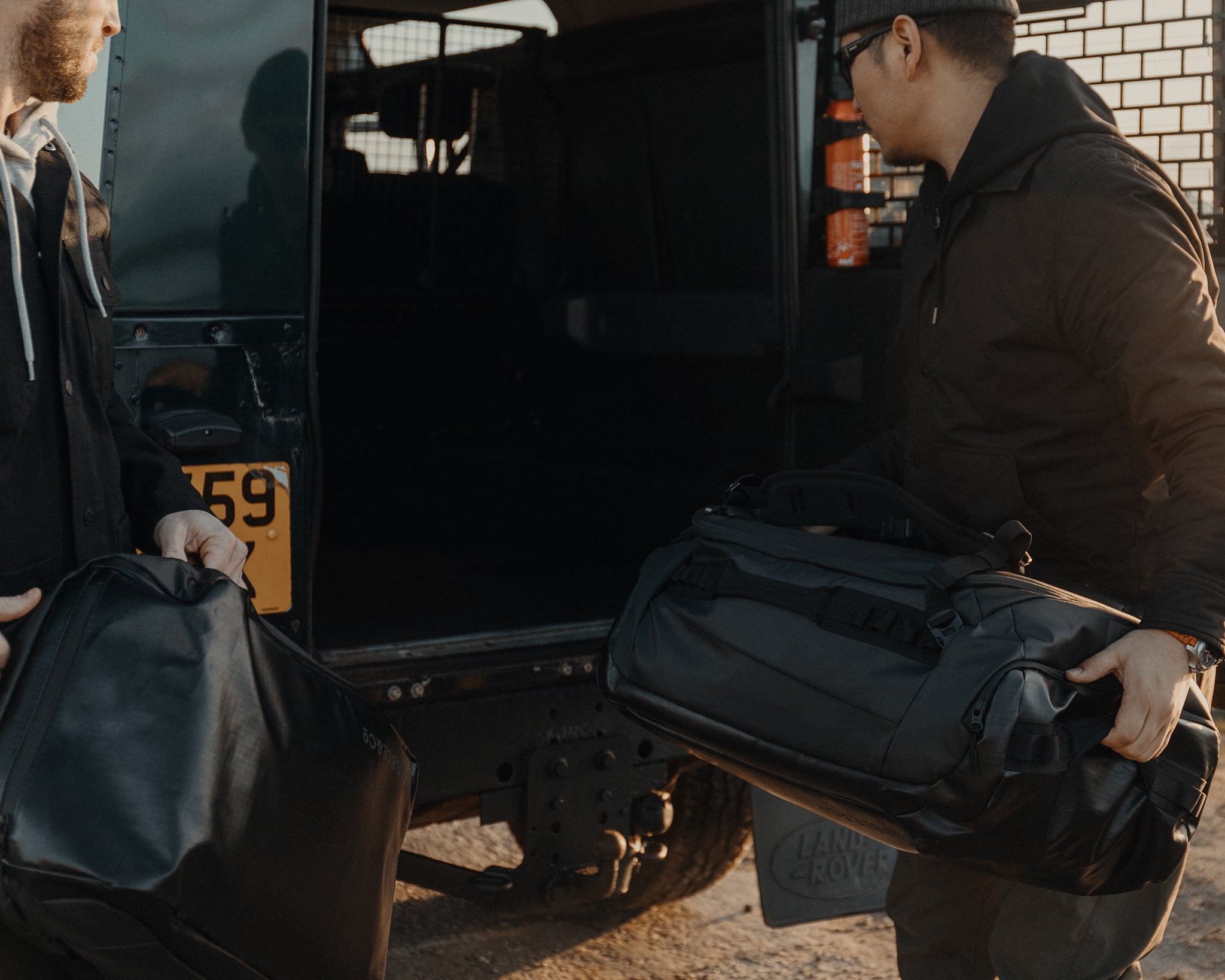 Two men are placing bags in the boot of a Land Rover on a trip. 