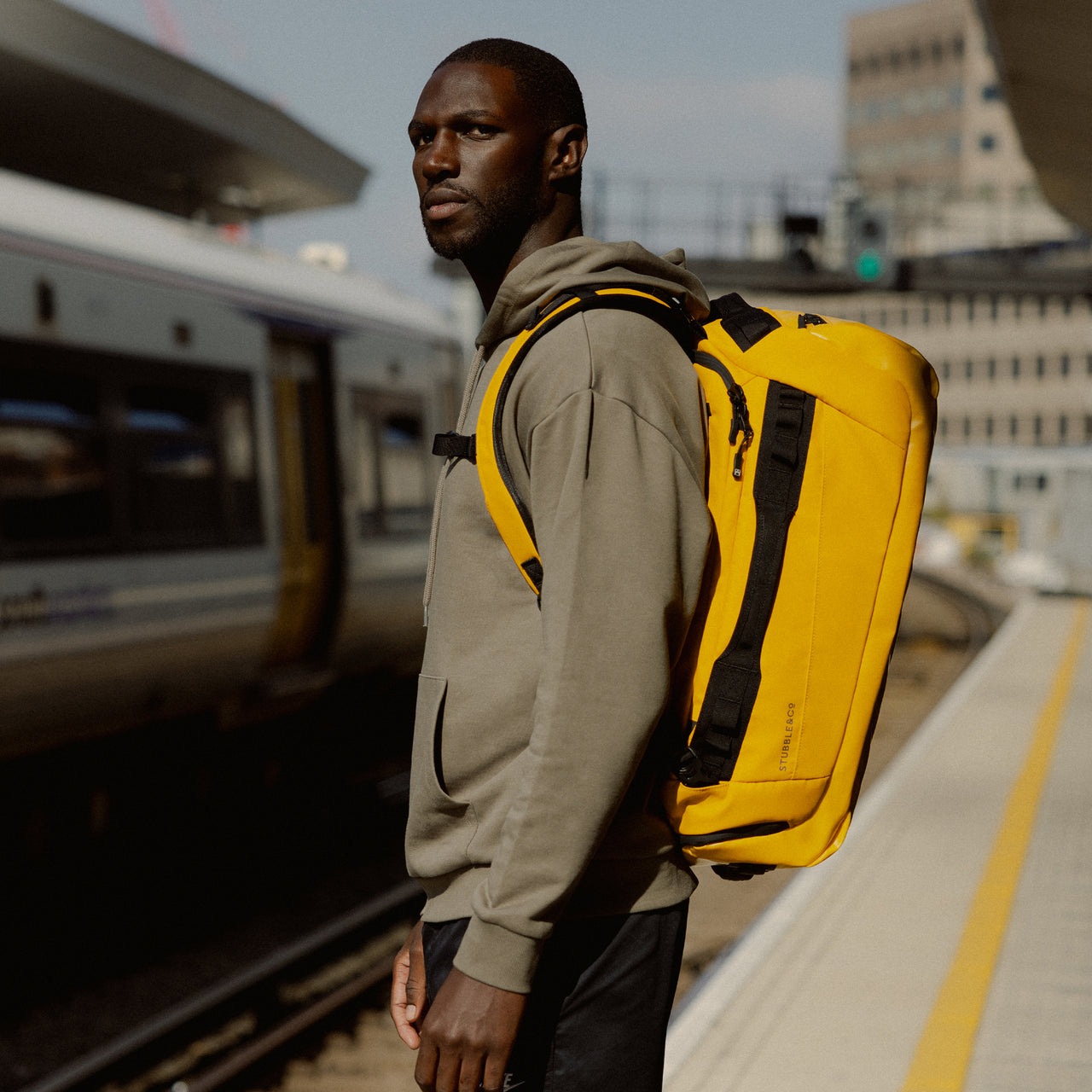 A man standing on a train station platform with a Kit Bag 40L in Yellow on his back