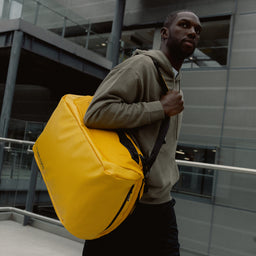 A man walking wearing a Kit Bag 40L in Yellow on his shoulder