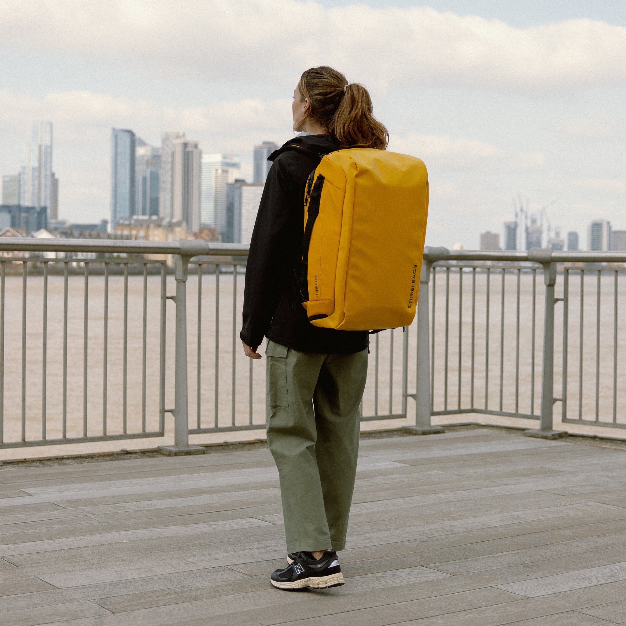 A woman standing by the river wearing a Kit Bag 40L in Yellow on her back