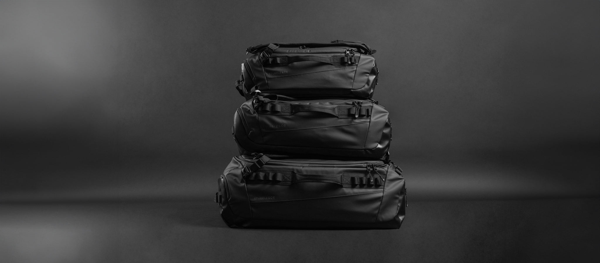 A studio shot of all three sizes of the Kit Bag black stacked on top of eachothe